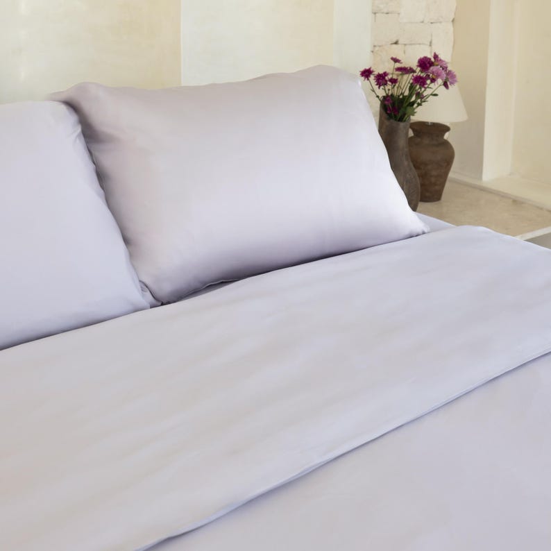 May include: A light gray bed with two pillows and a white duvet cover. The bed is made with crisp, clean linens.