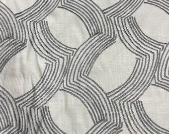 May include: Close-up of a white fabric with a repeating geometric pattern. The pattern consists of interlocking, curved shapes outlined with gray stitching. The fabric has a slightly textured appearance, suggesting a linen or similar material.