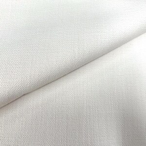 May include: Close-up of a folded, off-white fabric. The material has a textured weave, with visible threads creating a subtle pattern. The fabric is draped, showing folds and shadows that add depth to the image. The overall appearance is clean and simple.
