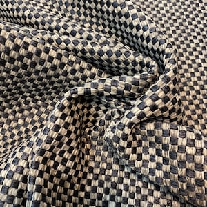 May include: Close-up of a woven fabric with a checkered pattern. The fabric features a repeating design of small, square blocks in shades of navy blue and off-white. The fabric is folded, showing texture and depth.