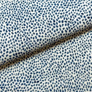 May include: White fabric with a repeating pattern of navy blue dots. The fabric is folded, showing the texture and design. The dots are irregularly spaced, creating a speckled appearance. This textile is suitable for various sewing projects.