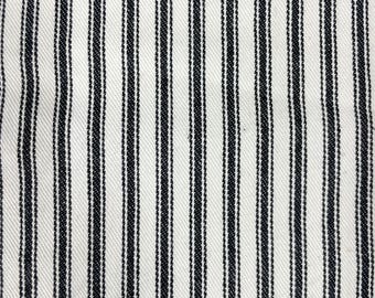 May include: Close-up of a white fabric with vertical black stripes. The stripes are evenly spaced and run the length of the fabric. The fabric has a textured appearance.
