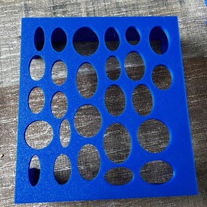 May include: A bright blue foam insert with various oval and circular cutouts. The cutouts are of different sizes and shapes, arranged in a grid pattern. The insert is designed to hold small objects, likely for organization or display.