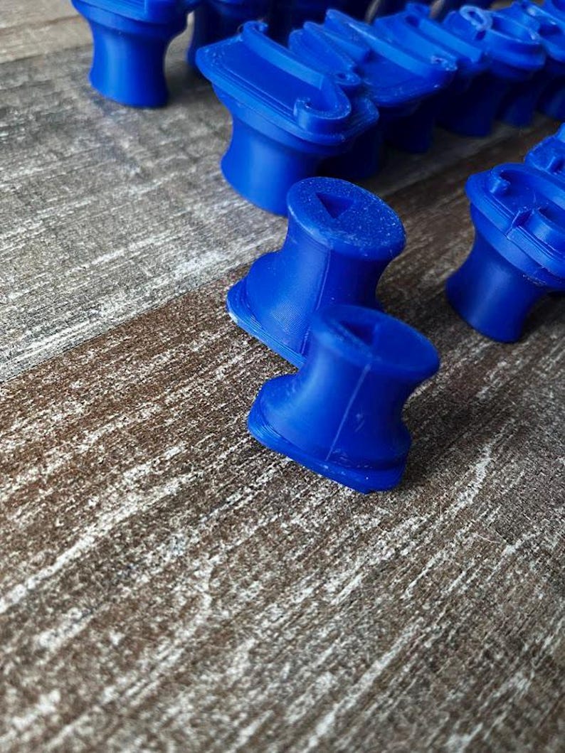 May include: Close-up of several bright blue, 3D-printed objects. The objects have a unique shape, with a cylindrical base and a wider top section. The objects are arranged on a textured, brown surface.