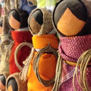 Pu&ograve; includere: Una collezione di bambole fatte a mano con accenti di tessuto colorato e spago. Le bambole sono fatte di juta e hanno volti e vestiti di diversi colori.