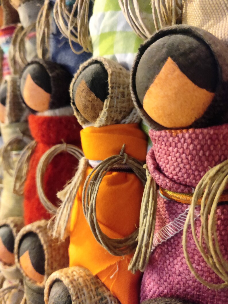 Pu&ograve; includere: Una collezione di bambole fatte a mano con accenti di tessuto colorato e spago. Le bambole sono fatte di juta e hanno volti e vestiti di diversi colori.