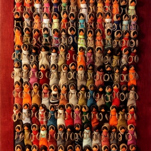 Pu&ograve; includere: Un'opera d'arte incorniciata che presenta una collezione di bambole di stoffa colorate disposte in file. Ogni bambola &egrave; unica, con motivi e colori diversi, creando una mostra vibrante e testurizzata.