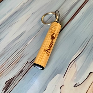 May include: A wooden keychain with a small flashlight and the name "Ariana" engraved on it.