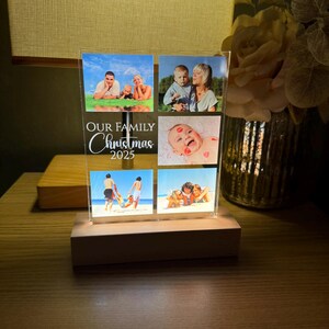 Puede incluir: Una pantalla de fotos de acr&iacute;lico transparente con seis fotos familiares, colocada sobre una base de madera. La pantalla presenta el texto "OUR FAMILY Christmas 2025" en escritura blanca. Las fotos representan a miembros de la familia en varios entornos.
