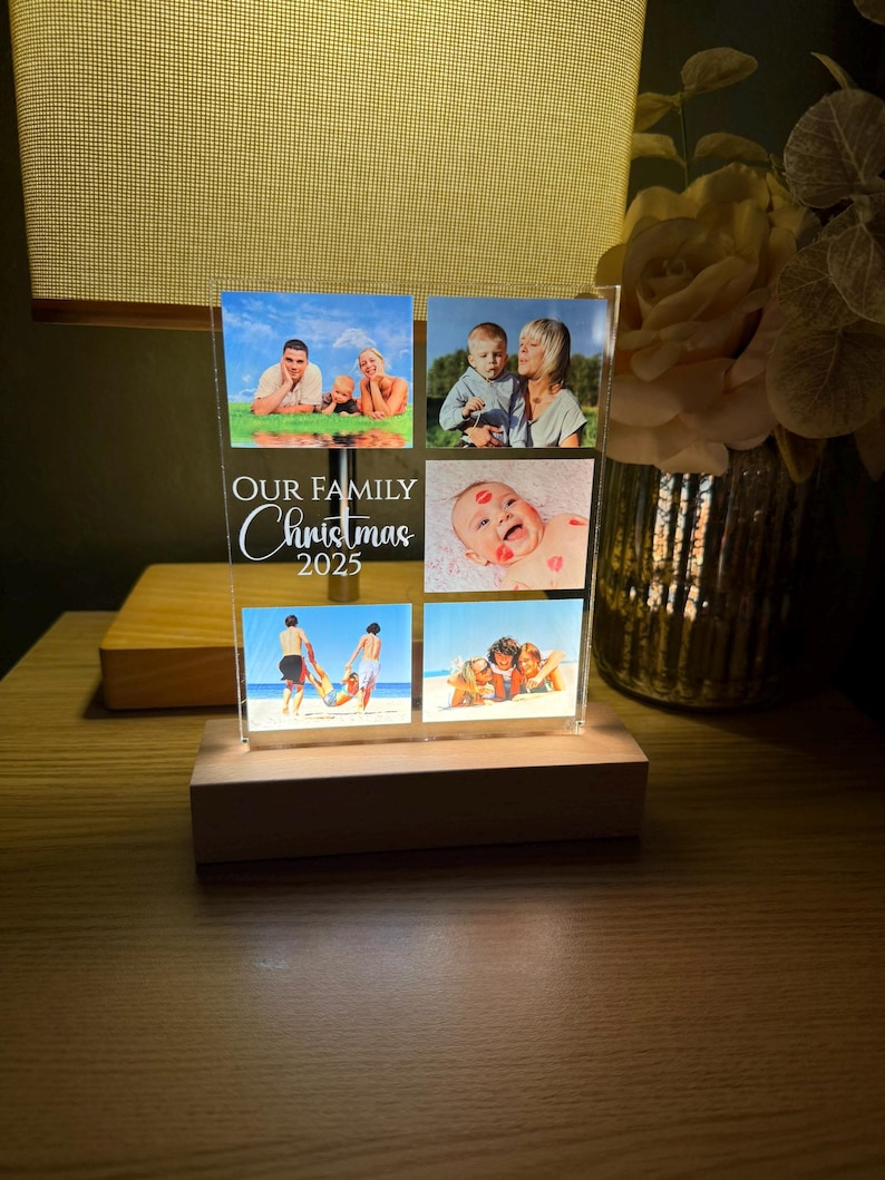 Puede incluir: Una pantalla de fotos de acr&iacute;lico transparente con seis fotos familiares, colocada sobre una base de madera. La pantalla presenta el texto "OUR FAMILY Christmas 2025" en escritura blanca. Las fotos representan a miembros de la familia en varios entornos.