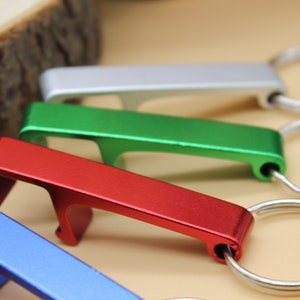 May include: Five bottle openers with key rings in different colors: silver, green, red, blue, and gold. The bottle openers are made of metal and have a simple design.
