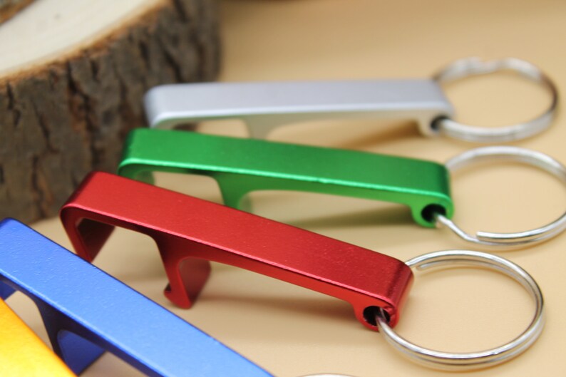 May include: Five bottle openers with key rings in different colors: silver, green, red, blue, and gold. The bottle openers are made of metal and have a simple design.