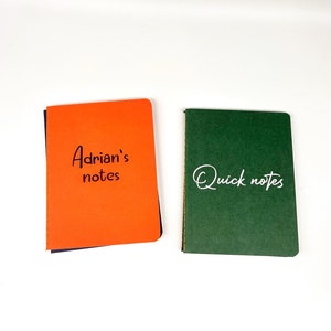 May include: Two small notebooks, one orange with the text "Adrian's notes" and one green with the text "Quick notes" in white.