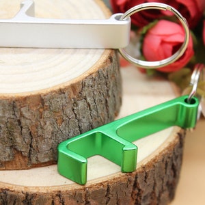 May include: Two bottle openers, one silver and one green, are shown on a wooden surface. The silver bottle opener is attached to a key ring.