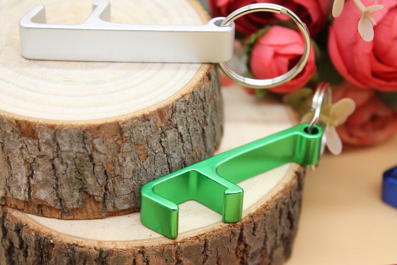 May include: Two bottle openers, one silver and one green, are shown on a wooden surface. The silver bottle opener is attached to a key ring.