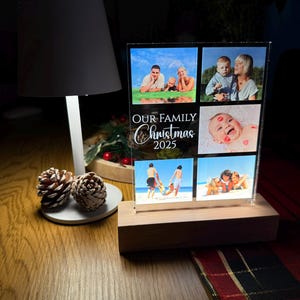 Puede incluir: Una pantalla fotogr&aacute;fica acr&iacute;lica transparente con una base de madera, con fotos familiares. La pantalla est&aacute; iluminada y tiene el texto "OUR FAMILY Christmas 2025". Las fotos muestran a una familia en la playa y en otros entornos.