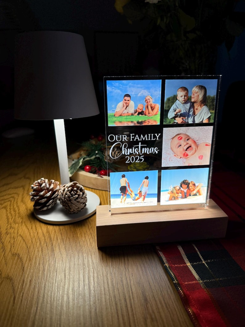 Puede incluir: Una pantalla fotogr&aacute;fica acr&iacute;lica transparente con una base de madera, con fotos familiares. La pantalla est&aacute; iluminada y tiene el texto "OUR FAMILY Christmas 2025". Las fotos muestran a una familia en la playa y en otros entornos.