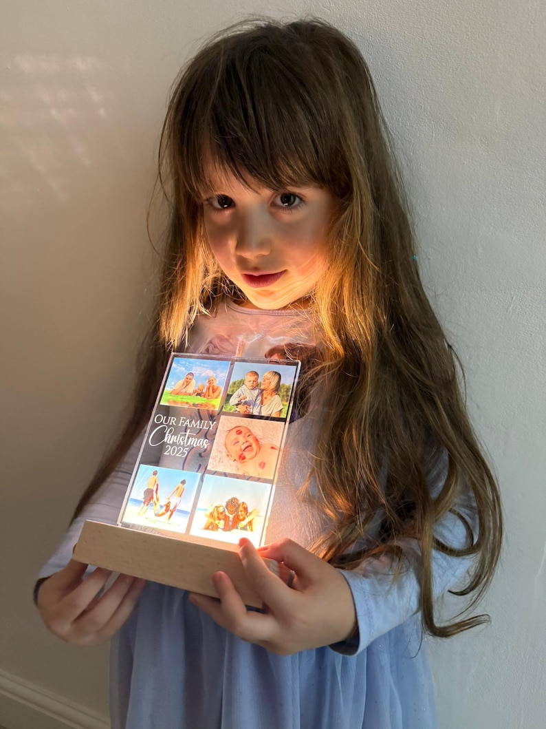 Puede incluir: Una pantalla fotogr&aacute;fica acr&iacute;lica iluminada con fotos familiares y el texto "OUR FAMILY Christmas 2025". La pantalla tiene una base de madera y la sostiene una persona. Las fotos son de una familia.