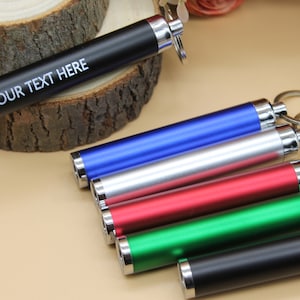 May include: Six different coloured keychain torches with a silver ring and a keyring. The black torch has the text "YOUR TEXT HERE" engraved on it.