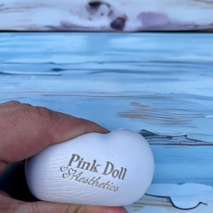 K&ouml;nnte beinhalten: Wei&szlig;er herzf&ouml;rmiger Stressball mit dem Aufdruck "Pink Doll Aesthetics".