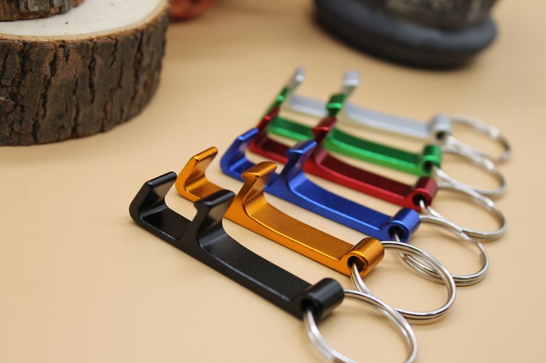 May include: A set of six keychains with bottle openers. The keychains are in different colors: black, gold, blue, red, green, and silver.