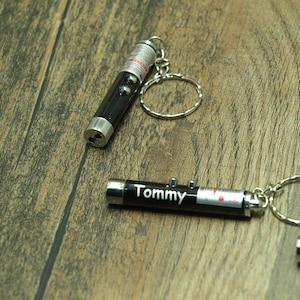 May include: Two black laser pointers with keyrings. One pointer has the name "Tommy" engraved on it.