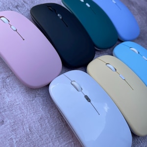 May include: A set of seven wireless computer mice in various colours, including pink, black, green, blue, light blue, white, and beige. The mice are all the same shape and size, and they have a simple, modern design.