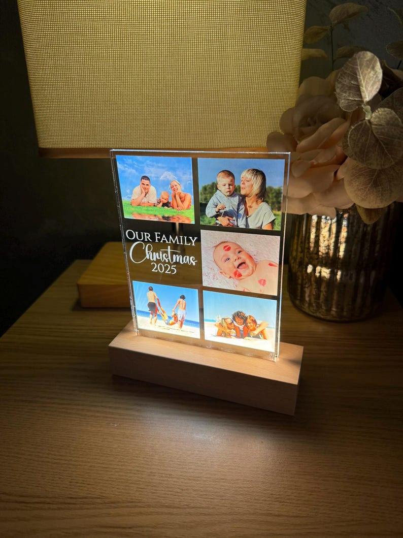 Puede incluir: Un expositor de fotos rectangular con cuatro fotos familiares, montado sobre una base de madera. El texto "OUR FAMILY CHRISTMAS 2023" est&aacute; impreso en la parte delantera. La pantalla est&aacute; iluminada desde abajo, creando un brillo c&aacute;lido.