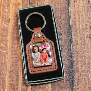 May include: A brown leather keyring with a silver frame photo insert featuring two young girls. The keyring is in a black velvet box.