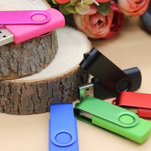 May include: Five different coloured USB flash drives. The drives are all in the shape of a rectangle with a rounded edge. The drives are all closed and ready to be used. The drives are on a wooden surface.