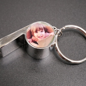 May include: Silver whistle keychain with a round photo insert featuring a young child smiling. The photo is set in a silver frame.