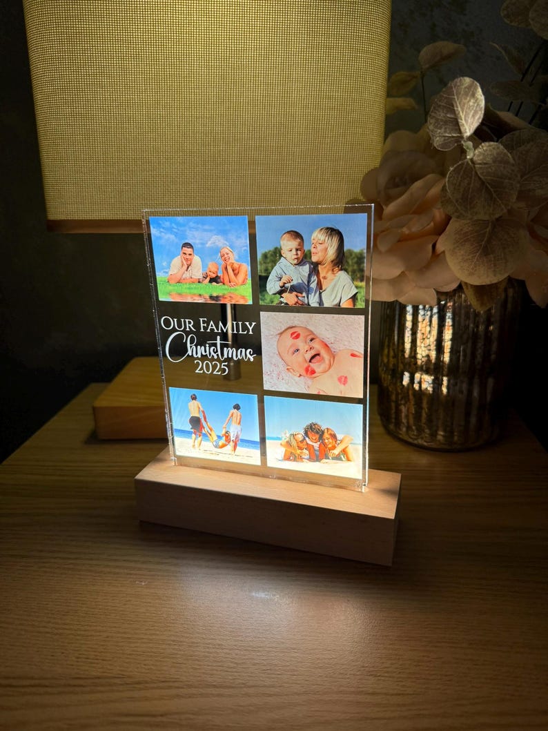 Puede incluir: Un expositor de fotos iluminado con cuatro fotos familiares. El texto "OUR FAMILY Christmas 2025" est&aacute; escrito en blanco. La base es de madera clara y las fotos est&aacute;n iluminadas desde dentro.