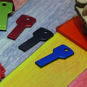 May include: Four key-shaped USB flash drives in different colors: green, red, black, and blue. The drives are arranged on a colorful wooden surface.