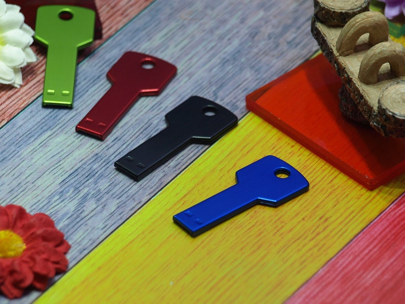 May include: Four key-shaped USB flash drives in different colors: green, red, black, and blue. The drives are arranged on a colorful wooden surface.