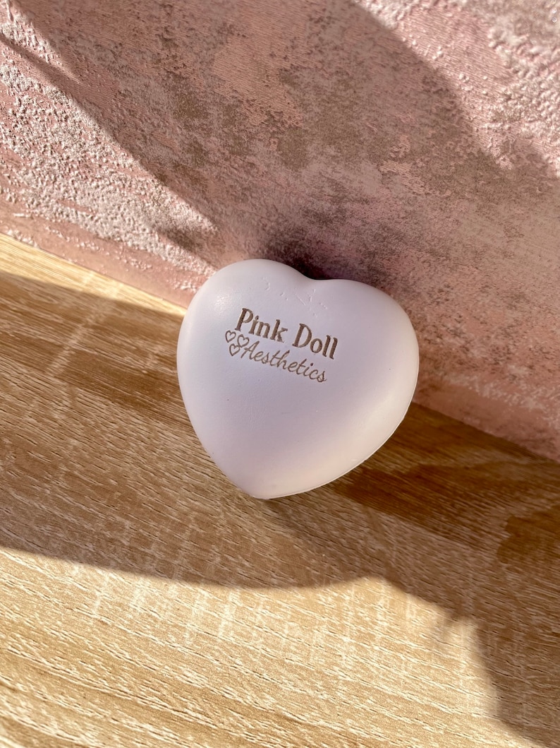 K&ouml;nnte beinhalten: Ein hellrosa, herzf&ouml;rmiges, weiches Spielzeug mit dem aufgedruckten Text "Pink Doll Aesthethics".