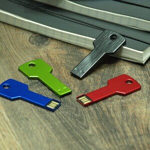 May include: Four key-shaped USB flash drives in different colors: black, green, blue, and red. The drives are on a wooden surface.