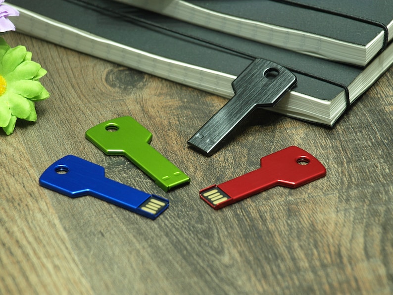 May include: Four key-shaped USB flash drives in different colors: black, green, blue, and red. The drives are on a wooden surface.