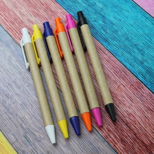 May include: Six pens with brown cardboard barrels and colored plastic tops. The pens are arranged in a row on a multi-colored wooden surface.