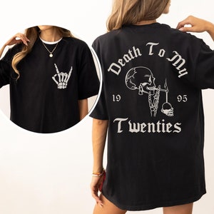 May include: A black t-shirt featuring a white skeleton hand making a rock-and-roll gesture on the front. The back displays a white graphic of a skeleton smoking with the text Death To My Twenties and the numbers 19 and 95 on either side.
