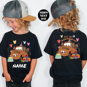 a young child wearing a black t-shirt with a cartoon character from the Cars movie, specifically a character named Wreck-It Ralph. The child is also wearing a baseball cap and a birthday hat, suggesting a birthday celebration theme.