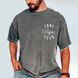 May include: A gray t-shirt with the text "Cool Papis Club" printed on the front in white.