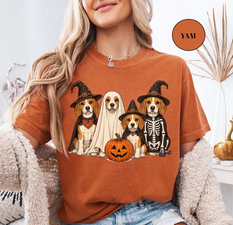 A woman wearing an orange t-shirt with a Halloween-themed graphic of four dogs dressed in costumes, including a ghost and a skeleton.