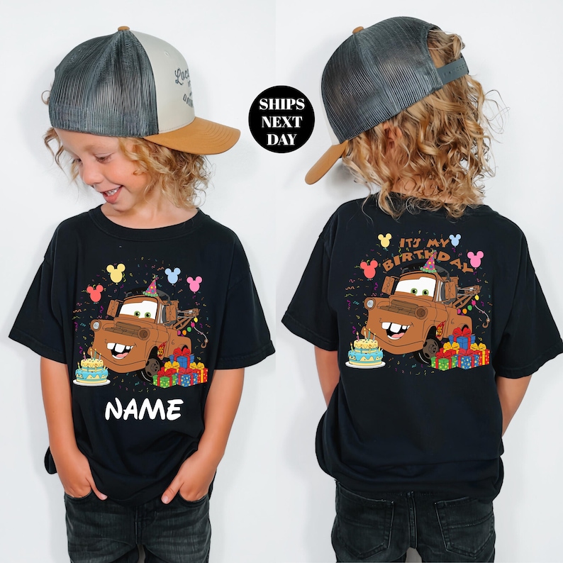 a young child wearing a black t-shirt with a cartoon character from the Cars movie, specifically a character named Wreck-It Ralph. The child is also wearing a baseball cap and a birthday hat, suggesting a birthday celebration theme.