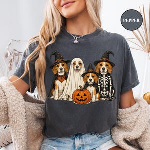 A woman wearing a t-shirt with a Halloween-themed graphic of four dogs dressed in costumes, including a ghost, skeleton, and pumpkin.