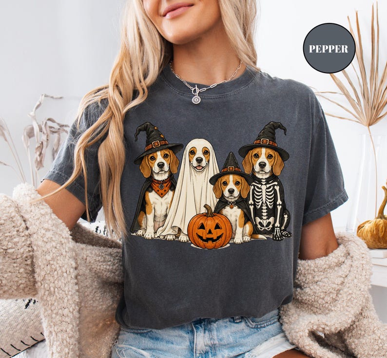 A woman wearing a t-shirt with a Halloween-themed graphic of four dogs dressed in costumes, including a ghost, skeleton, and pumpkin.