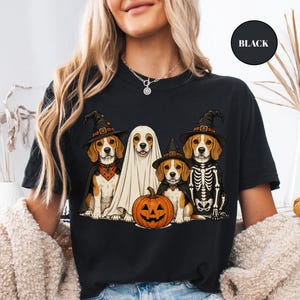 A woman wearing a black t-shirt with a Halloween-themed graphic of four dogs dressed in costumes, including a ghost, skeleton, and pumpkin.