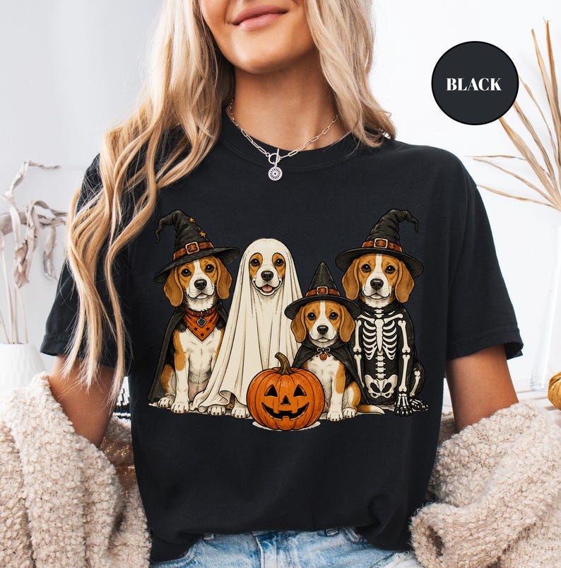 A woman wearing a black t-shirt with a Halloween-themed graphic of four dogs dressed in costumes, including a ghost, skeleton, and pumpkin.