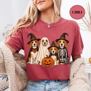 A woman wearing a red t-shirt with a graphic design of four dogs dressed in Halloween costumes, including a ghost, skeleton, and pumpkin.