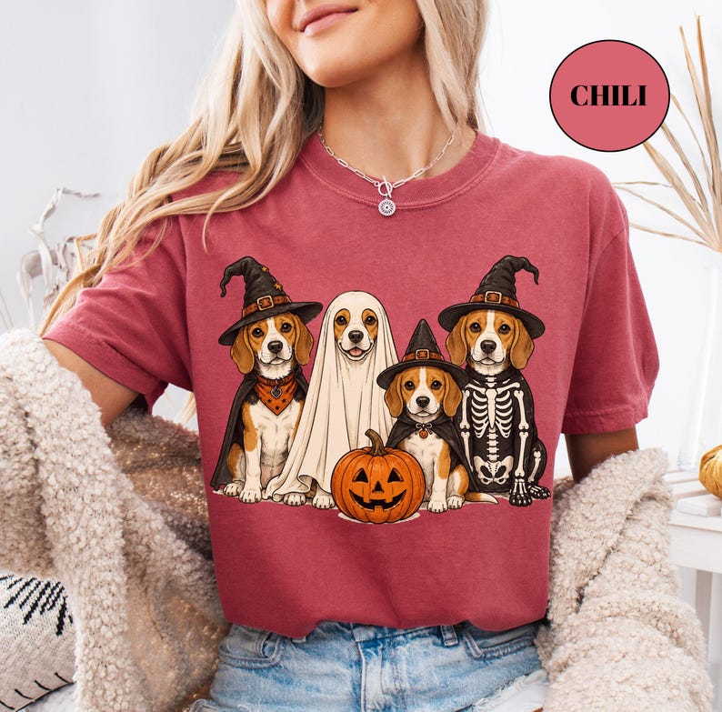 A woman wearing a red t-shirt with a graphic design of four dogs dressed in Halloween costumes, including a ghost, skeleton, and pumpkin.