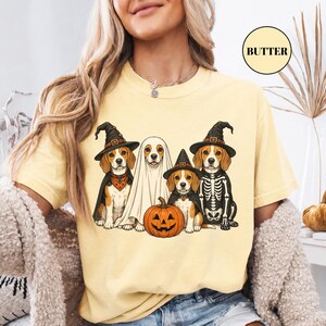 A woman wearing a yellow t-shirt with a graphic design of four dogs dressed in Halloween costumes, including a skeleton, a ghost, and a pumpkin.